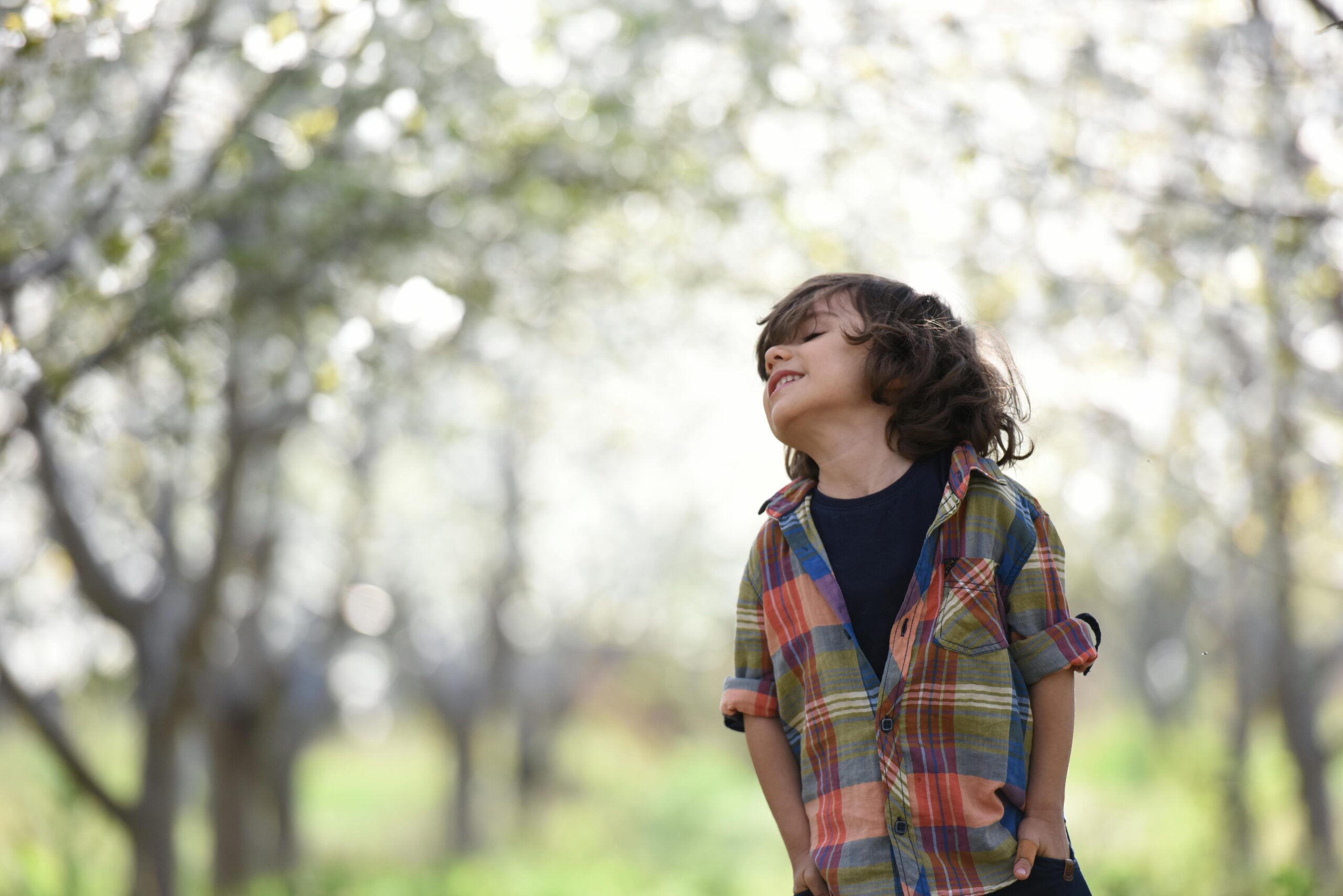 A joyful child in a colorful plaid shirt outdoors, enjoying a spring day.